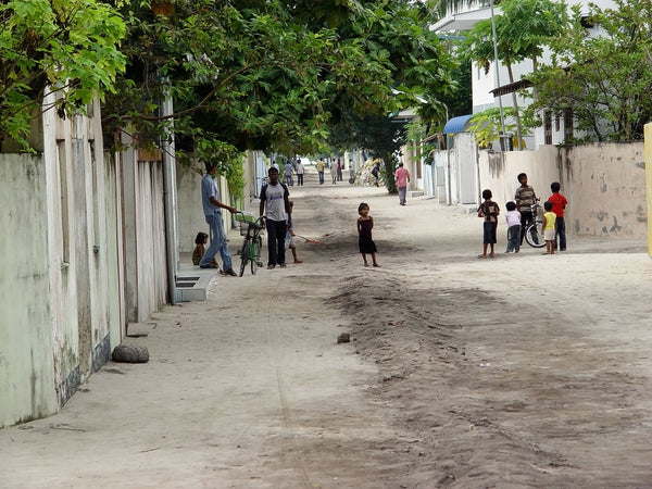 A sandy village street on Mahibadhoo lined with walls, trees and houses, with children playing