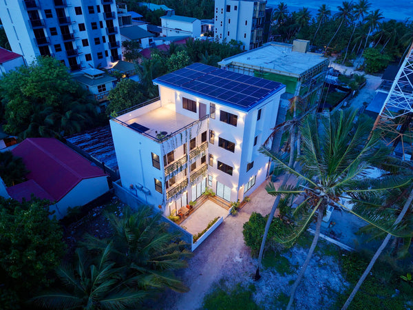 Cozy Art Dhangethi seen from the air at dusk, a white four-storey building lit among palm trees