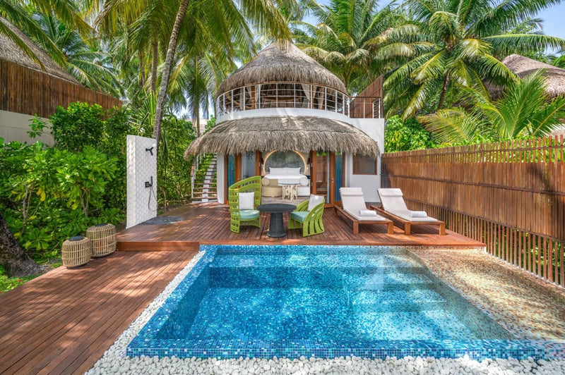 A beach villa at W Maldives, thatched pavilion and green loungers beside a walled garden pool.