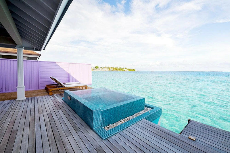 A water villa deck at The Standard Huruvalhi, a plunge pool against a purple wall facing a far island.