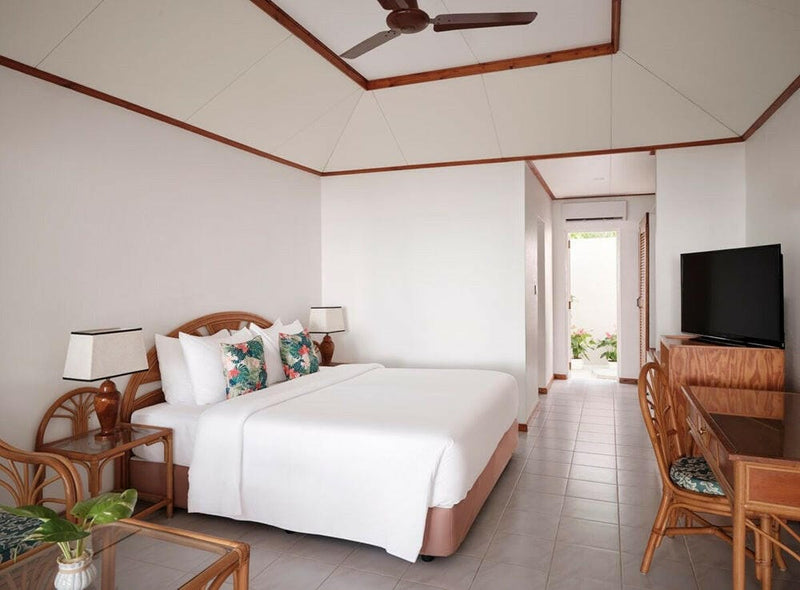 A beach villa room at Villa Park Sun Island, twin beds, a wall-mounted television and a cane dining set