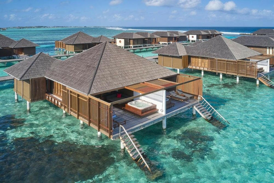Water villas at Villa Nautica from the air, grey pitched roofs on stilts above a bright turquoise lagoon.