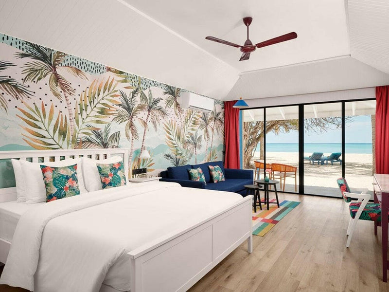 A beach villa bedroom at Villa Park Sun Island, leaf print wallpaper behind the bed and a navy sofa