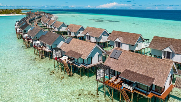 The overwater villas at OZEN LIFE Maadhoo from the air, a long line of thatched villas on stilts above the shallows