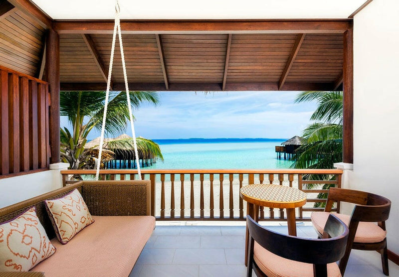 A Beach Front Deluxe Room balcony at Sheraton Maldives Full Moon, a cushioned sofa looking to the water villas.