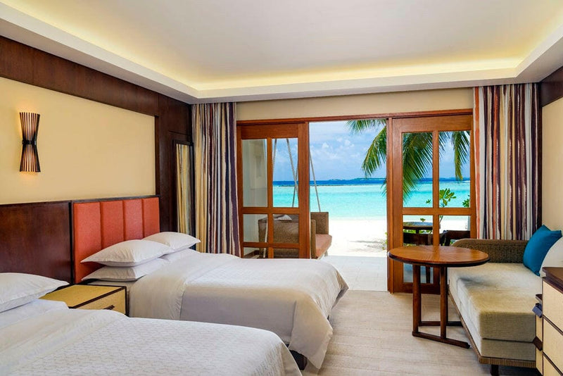 A Beach Front Deluxe Room at Sheraton Maldives Full Moon, twin beds with red headboards facing balcony doors.