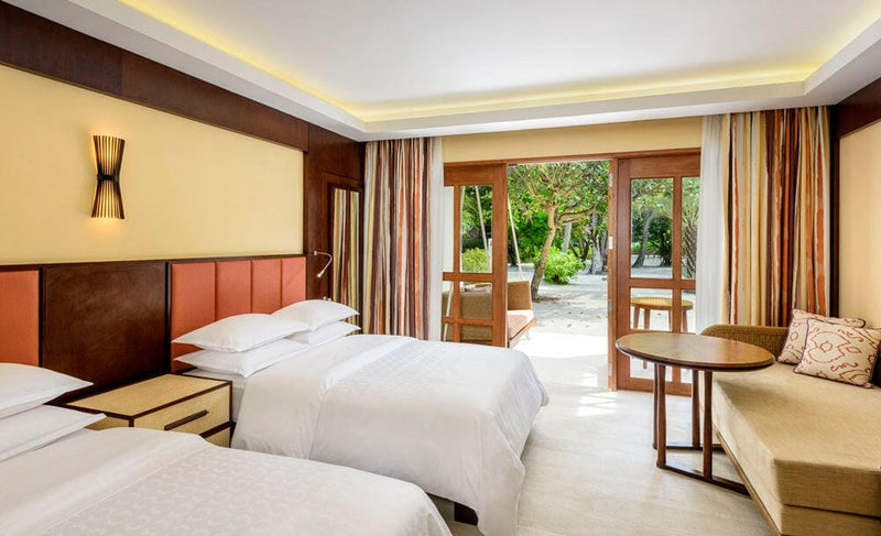 A Deluxe Room at Sheraton Maldives Full Moon, twin beds and a sofa with doors through to the garden.
