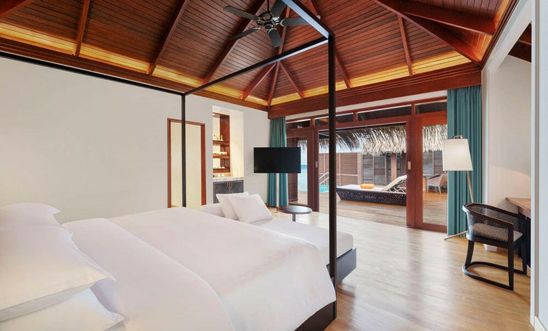 A water villa bedroom at Sheraton Maldives Full Moon, a four poster bed beneath a high timber ceiling.