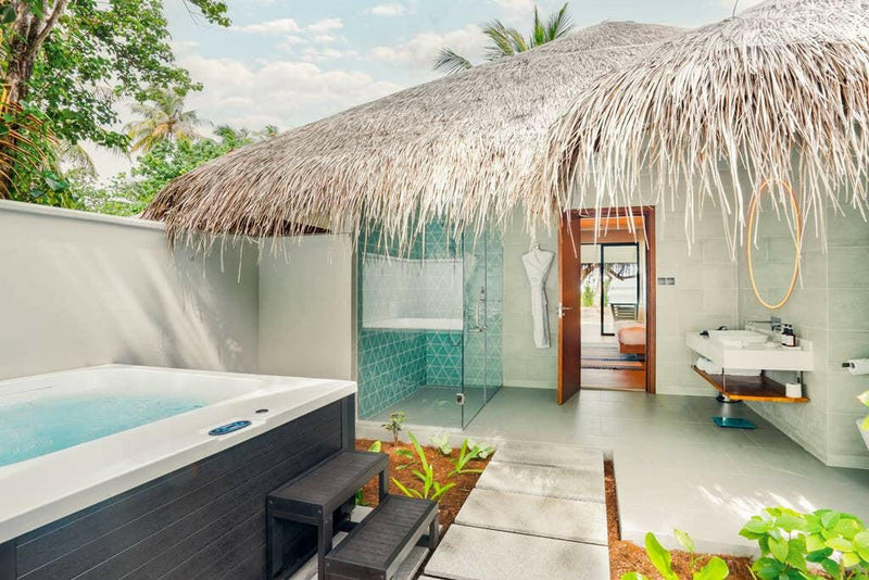 A garden jacuzzi at Nova Maldives under a thatched roof, with a washbasin and green tiles beyond.
