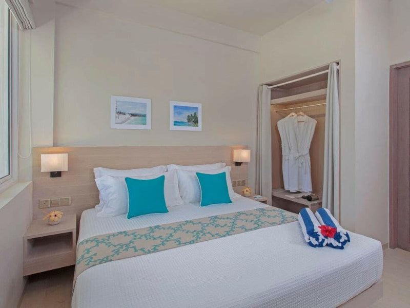 A Superior Room at Malahini Kuda Bandos with a king bed, two framed beach prints and robes in the open wardrobe.