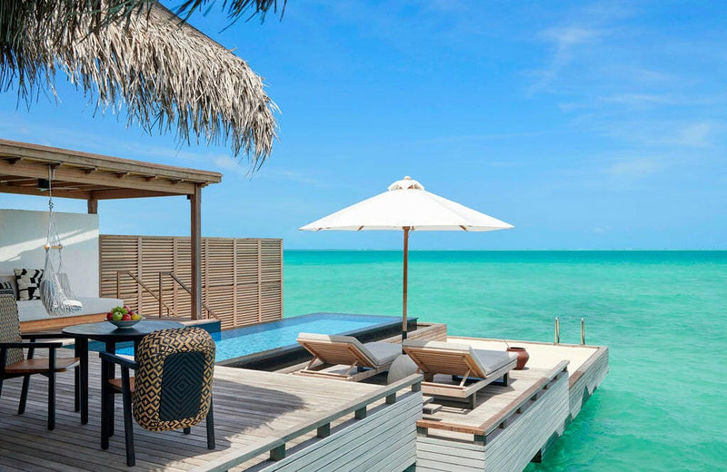 A water villa deck at Sirru Fen Fushi, dining table and plunge pool above green turquoise water.