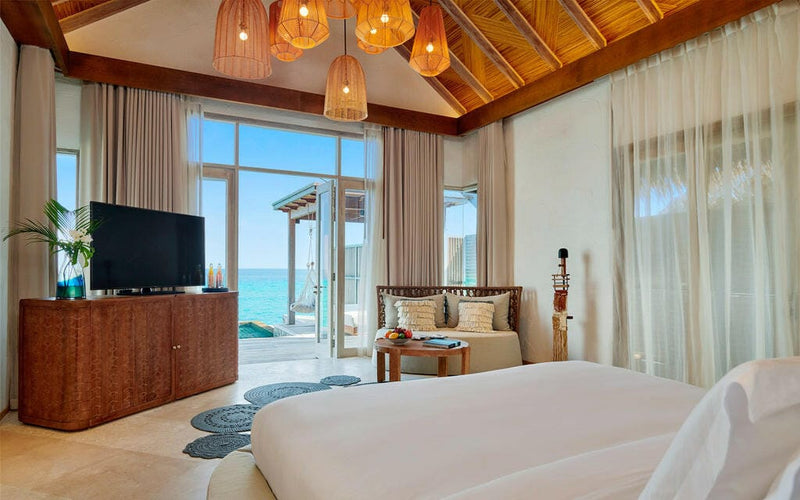 A water villa bedroom at Sirru Fen Fushi, copper pendant lights and doors onto the turquoise lagoon.