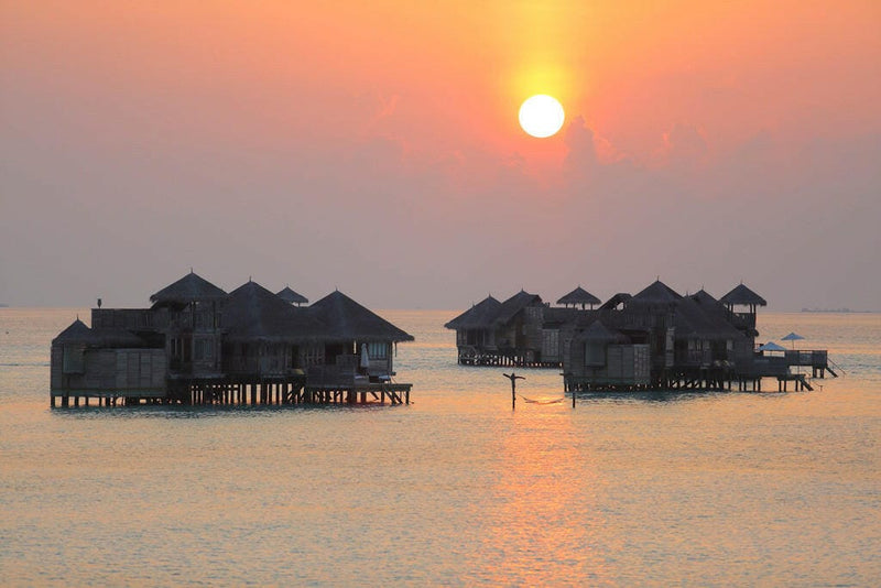 Overwater villas at Gili Lankanfushi silhouetted against an orange sky as the sun drops to the sea.