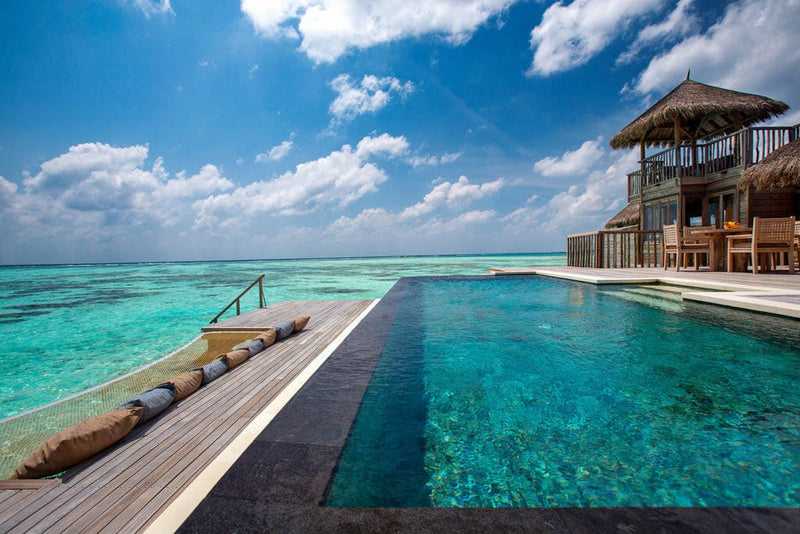 A deck-level infinity pool at Gili Lankanfushi, its edge meeting the lagoon beside a thatched villa.