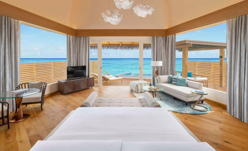 A villa bedroom at JW Marriott Maldives, timber floor and wide glass doors framing the open lagoon.