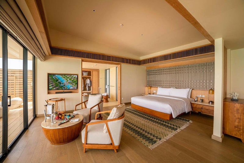 A villa bedroom at Kuda Villingili, terracotta throw on the bed and two armchairs by the terrace.