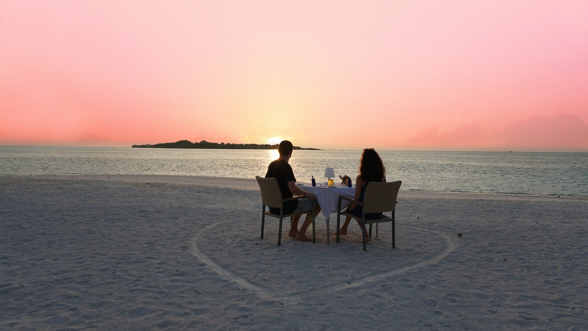 A couple dining on the sand at sunset at Cocoon Maldives in Lhaviyani Atoll