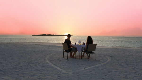 A couple dining on the sand at sunset at Cocoon Maldives in Lhaviyani Atoll