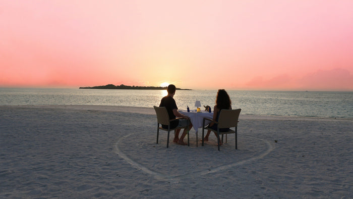 A couple dining on the sand at sunset at Cocoon Maldives in Lhaviyani Atoll