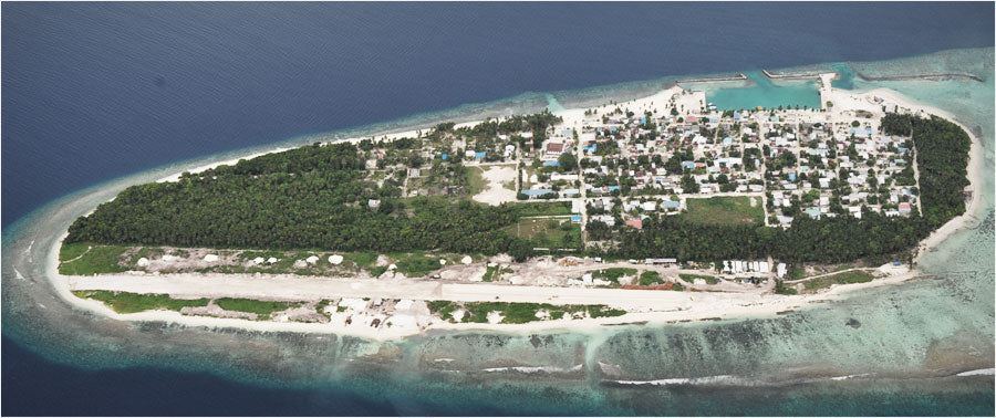 Dharavandhoo from the air, a green island with a village, harbour and airstrip in Baa Atoll