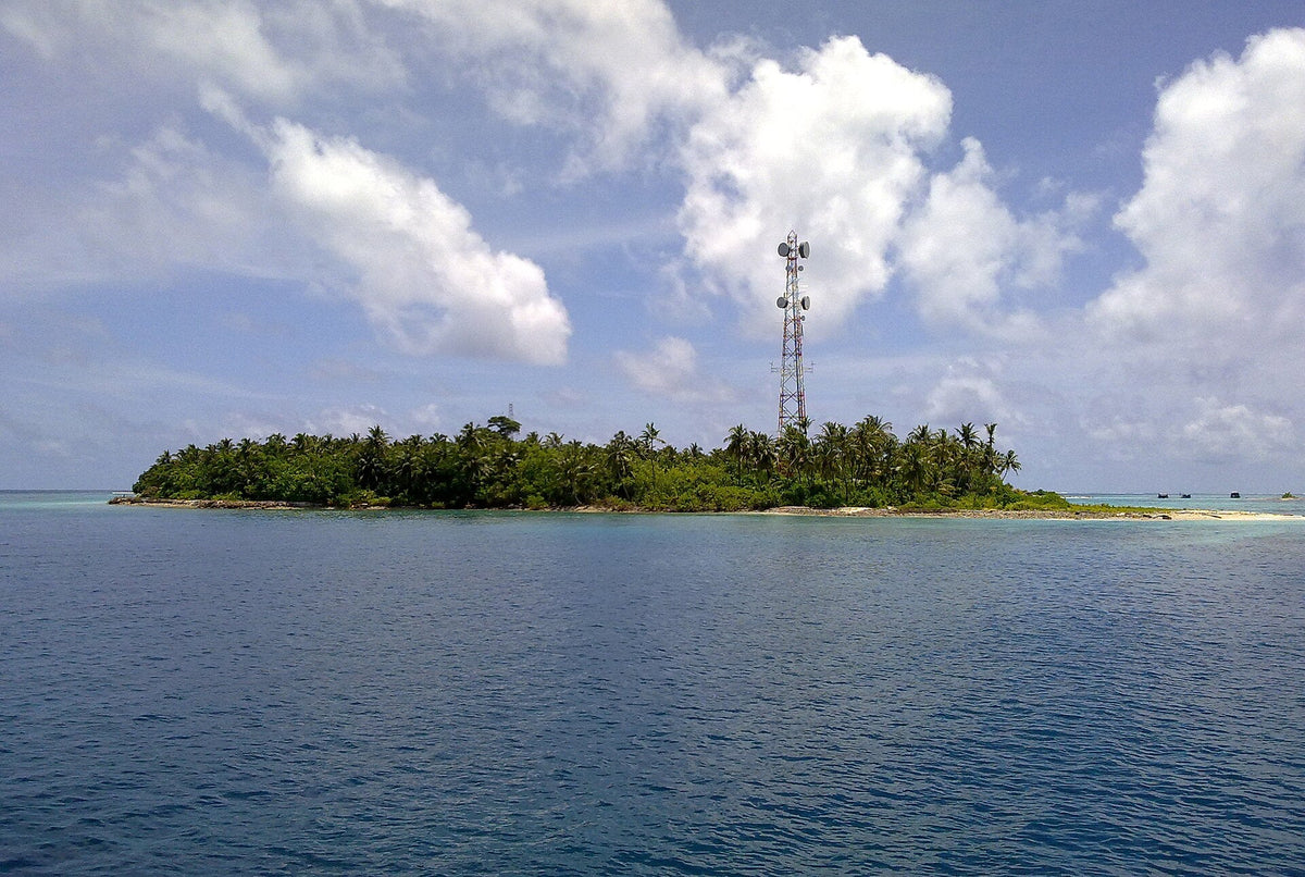 Himandhoo seen from the sea, a low green island with a communications mast under a blue sky
