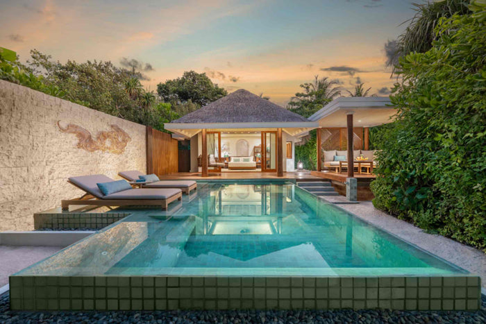 A Beach Pool Villa at Anantara Kihavah Maldives Villas in Baa Atoll at sunset, loungers beside the pool with the sala lit alongside