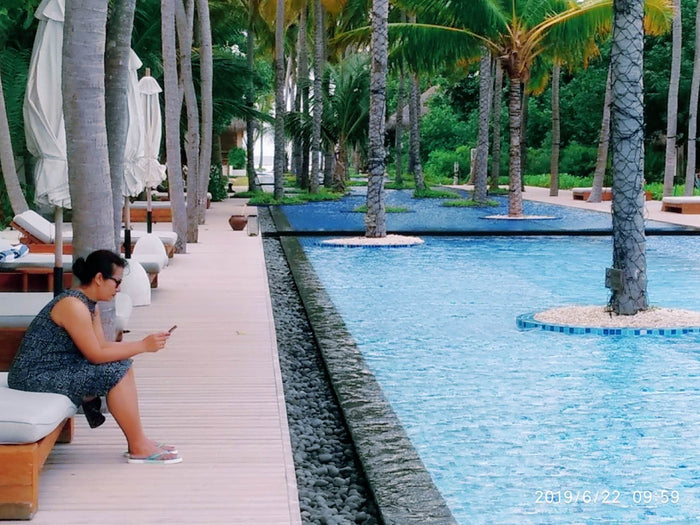 A woman sitting beside a long, palm-lined reflecting pool at Sirru Fen Fushi