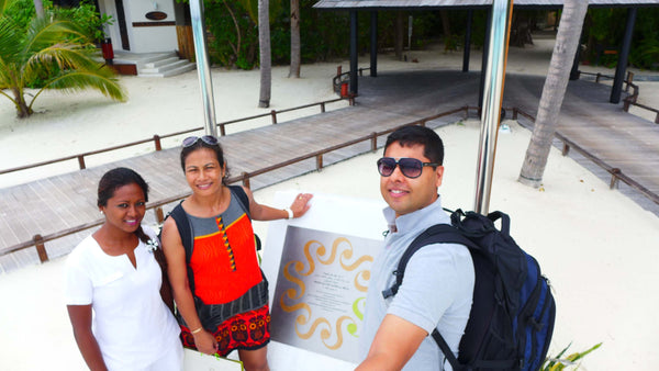Three people, one of them resort staff, holding a welcome plaque on the sand at Sun Siyam Iru Fushi