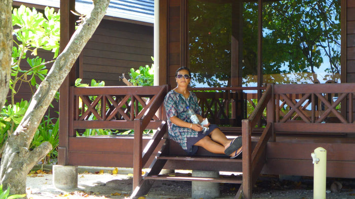 A woman sitting on the timber steps of a villa veranda at Royal Island, shaded by trees