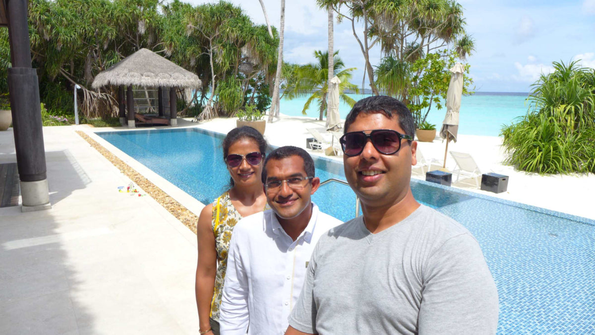 Selfie of three people beside a long swimming pool at Velaa Private Island Maldives, with a thatched sala and the beach behind