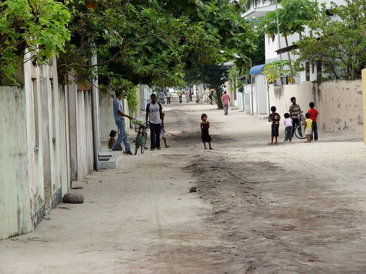 A sandy village street on Mahibadhoo lined with walls, trees and houses, with children playing