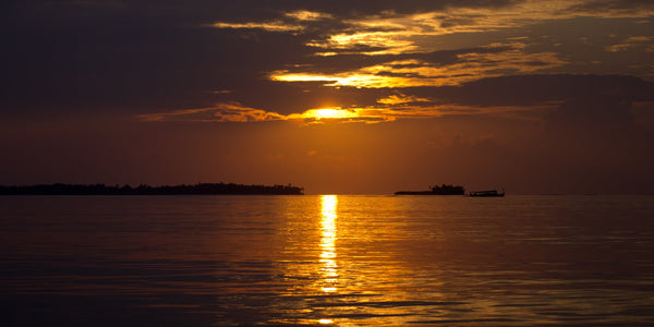 The sun rising through clouds over calm water and low islands in southern Ari Atoll