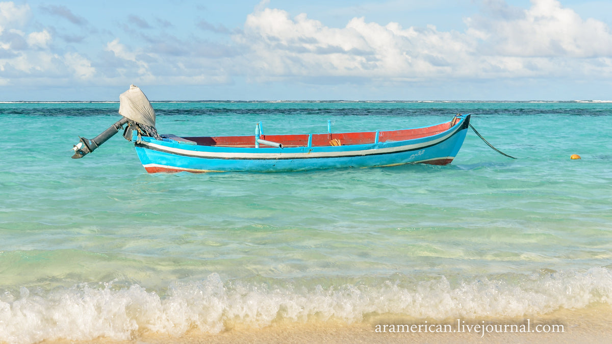 A small boat moored in the turquoise shallows off a white beach on Thoddoo