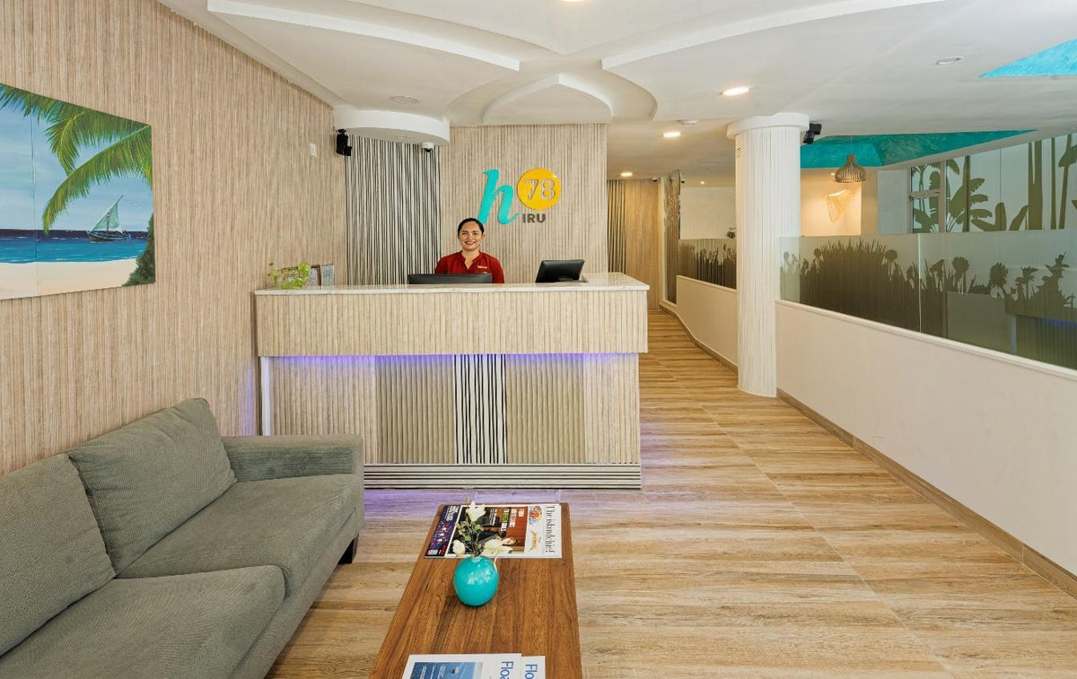 h78 Iru Hulhumalé, North Malé Atoll: reception desk with the h78 Iru sign, a grey sofa in the lobby and a wooden-floored corridor