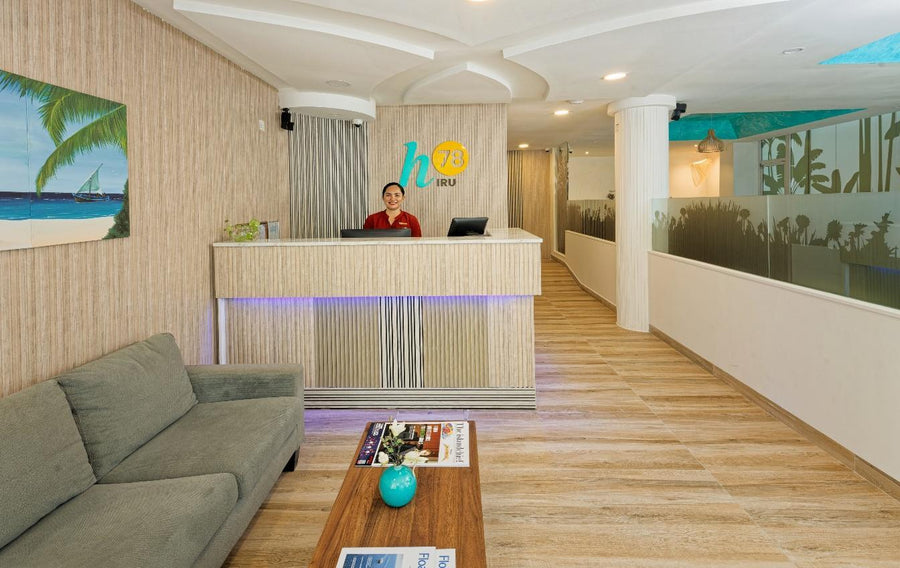 h78 Iru Hulhumalé, North Malé Atoll: reception desk with the h78 Iru sign, a grey sofa in the lobby and a wooden-floored corridor