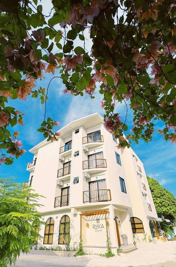 Ruka Maldives Dhiffushi, North Malé Atoll: the white five-storey guest house with balconies and the Ruka sign, seen through bougainvillea