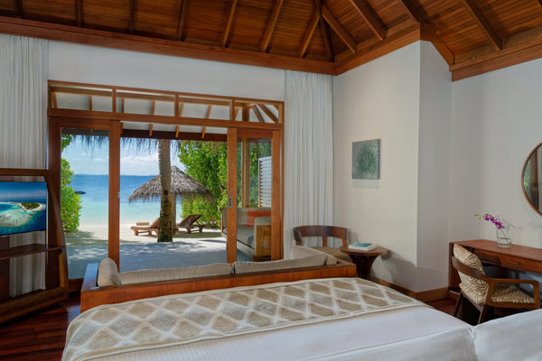 A Deluxe Beach Villa bedroom at Baros Maldives, doors open onto the beach and the sea.