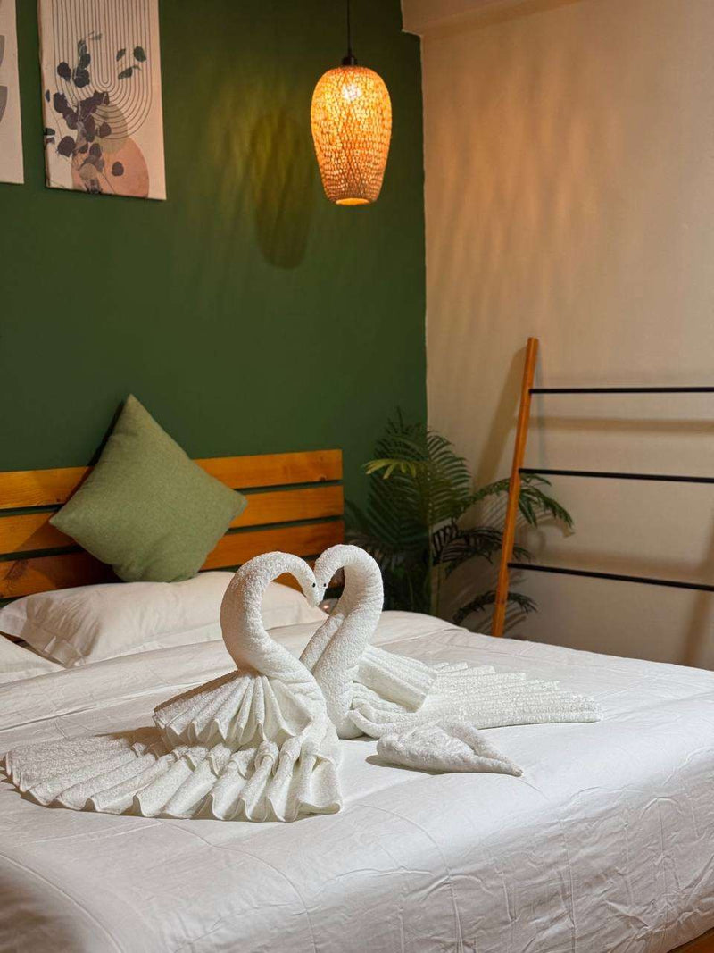 Ruka Maldives Dhiffushi, North Malé Atoll: Premium Room with a king bed, towel swans, a green wall and a woven pendant lamp