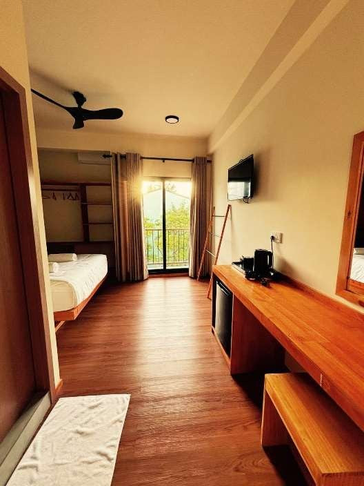 Ruka Maldives Dhiffushi, North Malé Atoll: Premium Room with Bathtub, a long room with a wooden desk, a bed and a balcony door at the far end