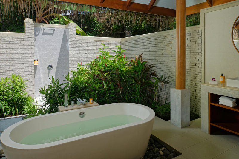 The outdoor bathroom of a Deluxe Beach Villa at Baros Maldives, a freestanding tub in a walled garden.