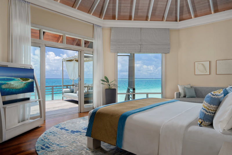 A Water Villa bedroom at Baros Maldives, glass doors opening onto the deck and the lagoon.
