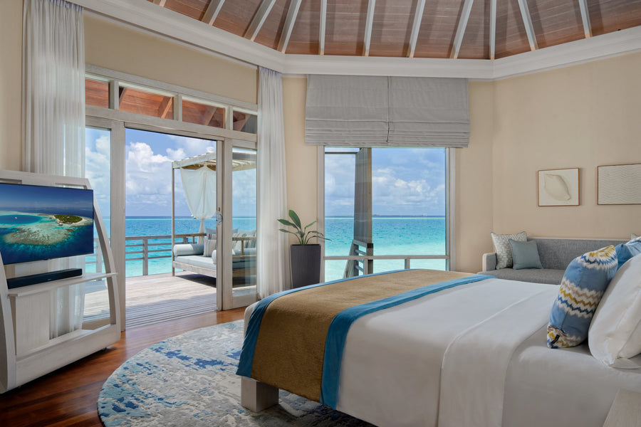 A Water Villa bedroom at Baros Maldives, glass doors opening onto the deck and the lagoon.
