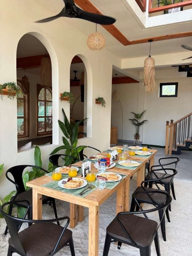 Ruka Maldives Dhiffushi, North Malé Atoll: breakfast laid on a long wooden table under white arches, with plants and pendant lights