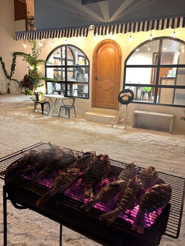Ruka Maldives Dhiffushi, North Malé Atoll: fish on a barbecue grill in the sand courtyard at night, arched windows and a wooden door behind