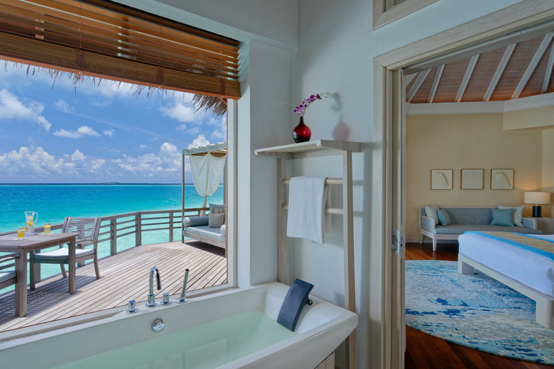 A Water Villa bathroom at Baros Maldives, a bathtub at a window looking across the deck to the sea.