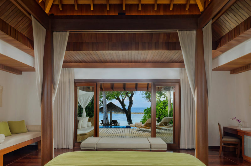 A Baros Pool Villa bedroom at Baros Maldives, a curtained four-poster bed facing doors to the garden terrace.