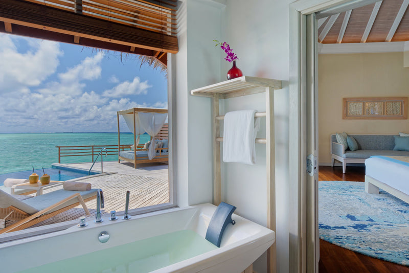 A Water Pool Villa bathroom at Baros Maldives, a tub at the window with the plunge pool and daybed on the deck beyond.