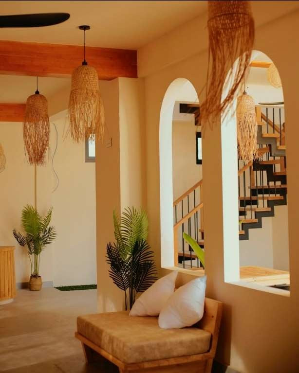 Ruka Maldives Dhiffushi, North Malé Atoll: lobby lounge with a cushioned bench, woven pendant lights, white arches and a wooden staircase