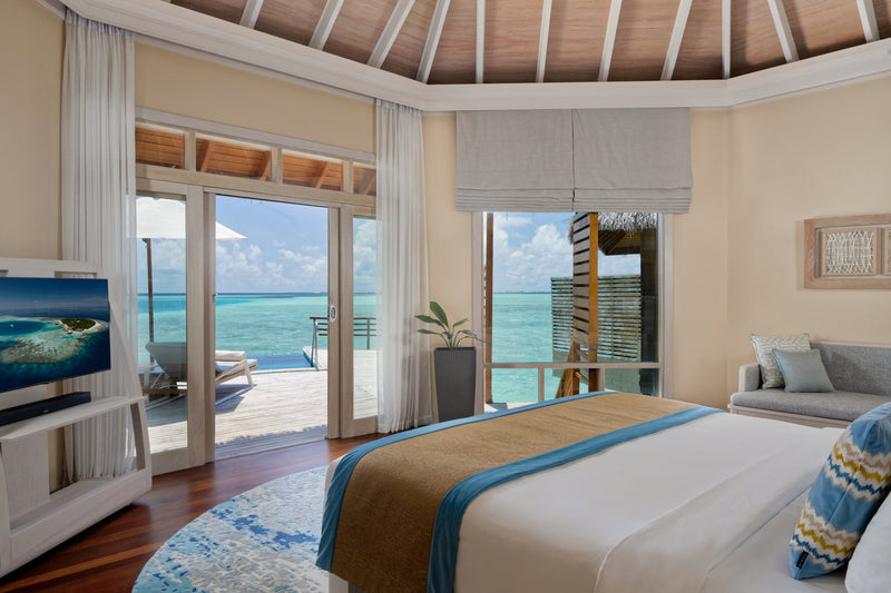 A Water Pool Villa bedroom at Baros Maldives, the bed facing glass doors onto the deck and the open sea.