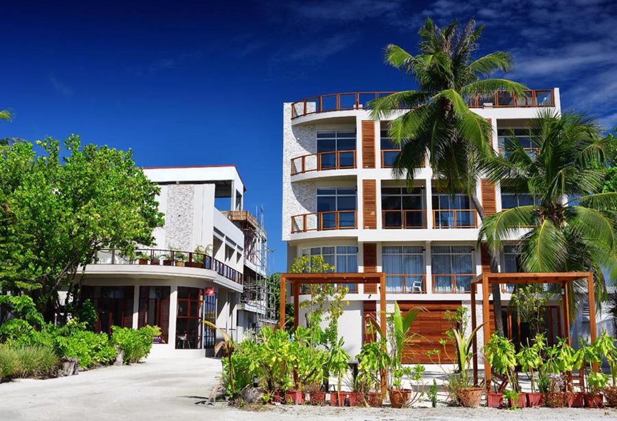 Velana Beach Hotel, a white building with balconies behind palm trees on Maafushi